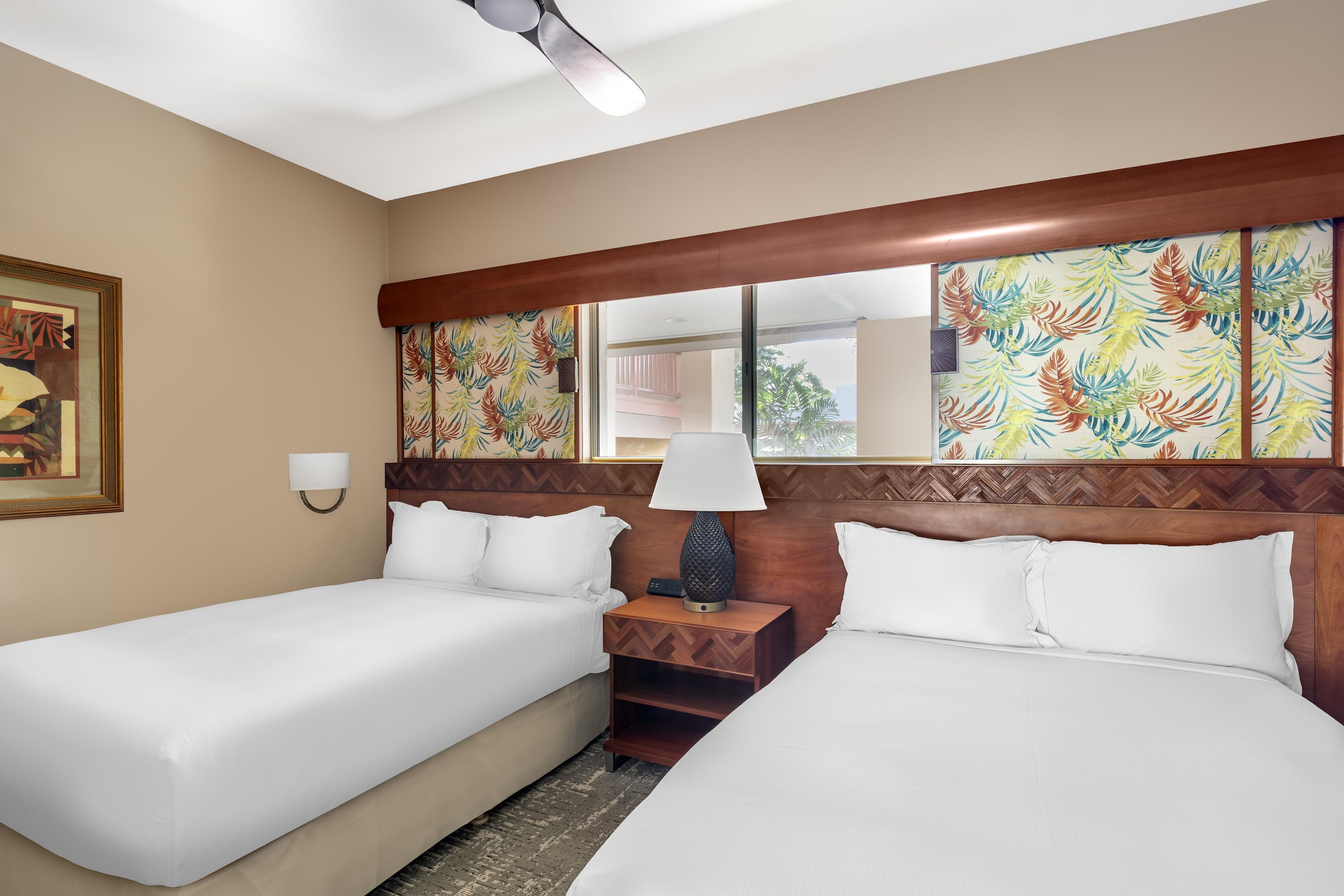 A hotel room with two single beds, a nightstand with a lamp, a large mirror, and a painting on the wall.