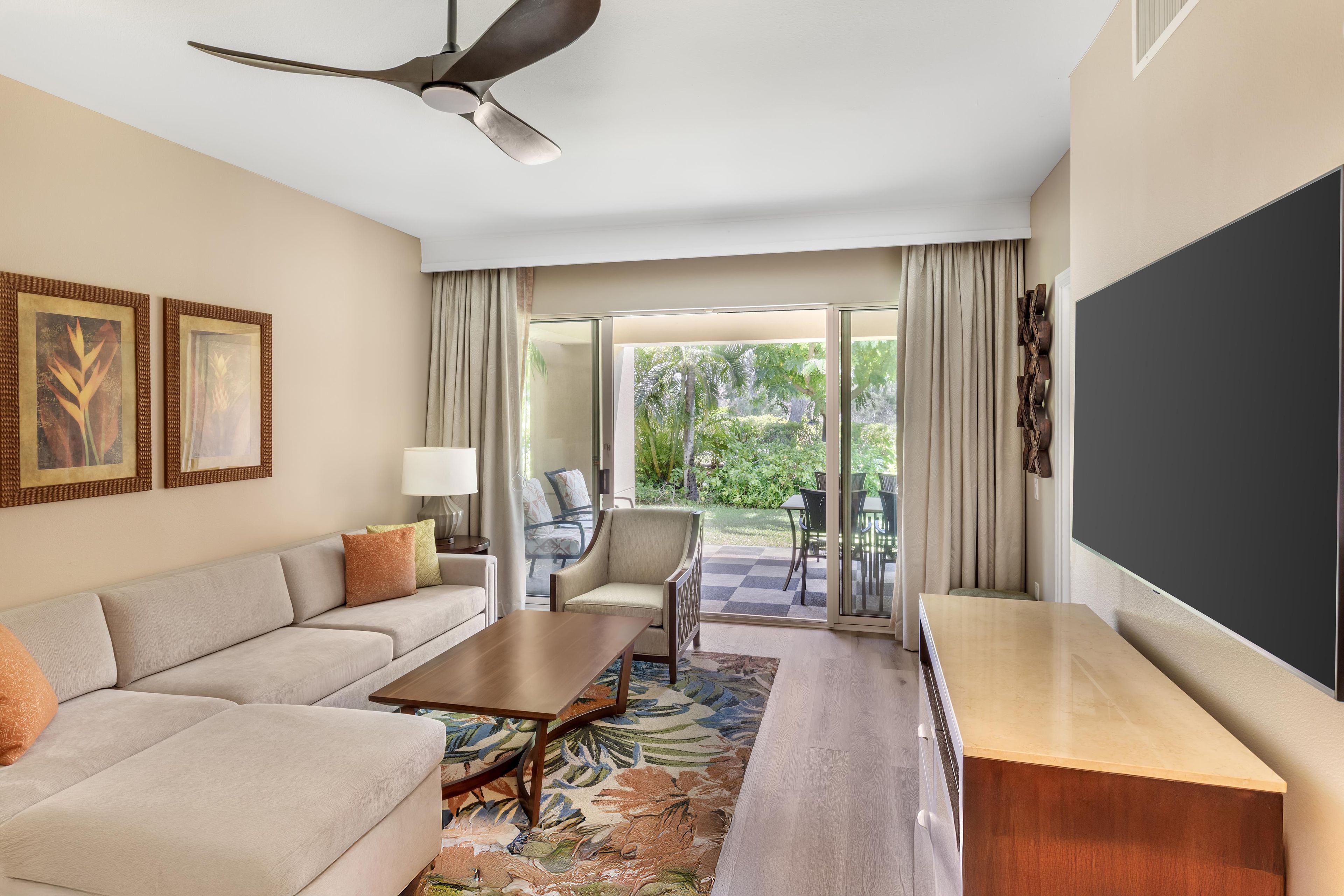 A hotel room with a sofa, a coffee table, a TV, and a balcony with outdoor furniture.