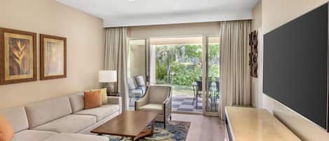 A hotel room with a sofa, a coffee table, a TV, and a balcony with outdoor furniture.