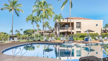 A resort with a pool, lounge chairs, palm trees, and a building with a tiled roof.
