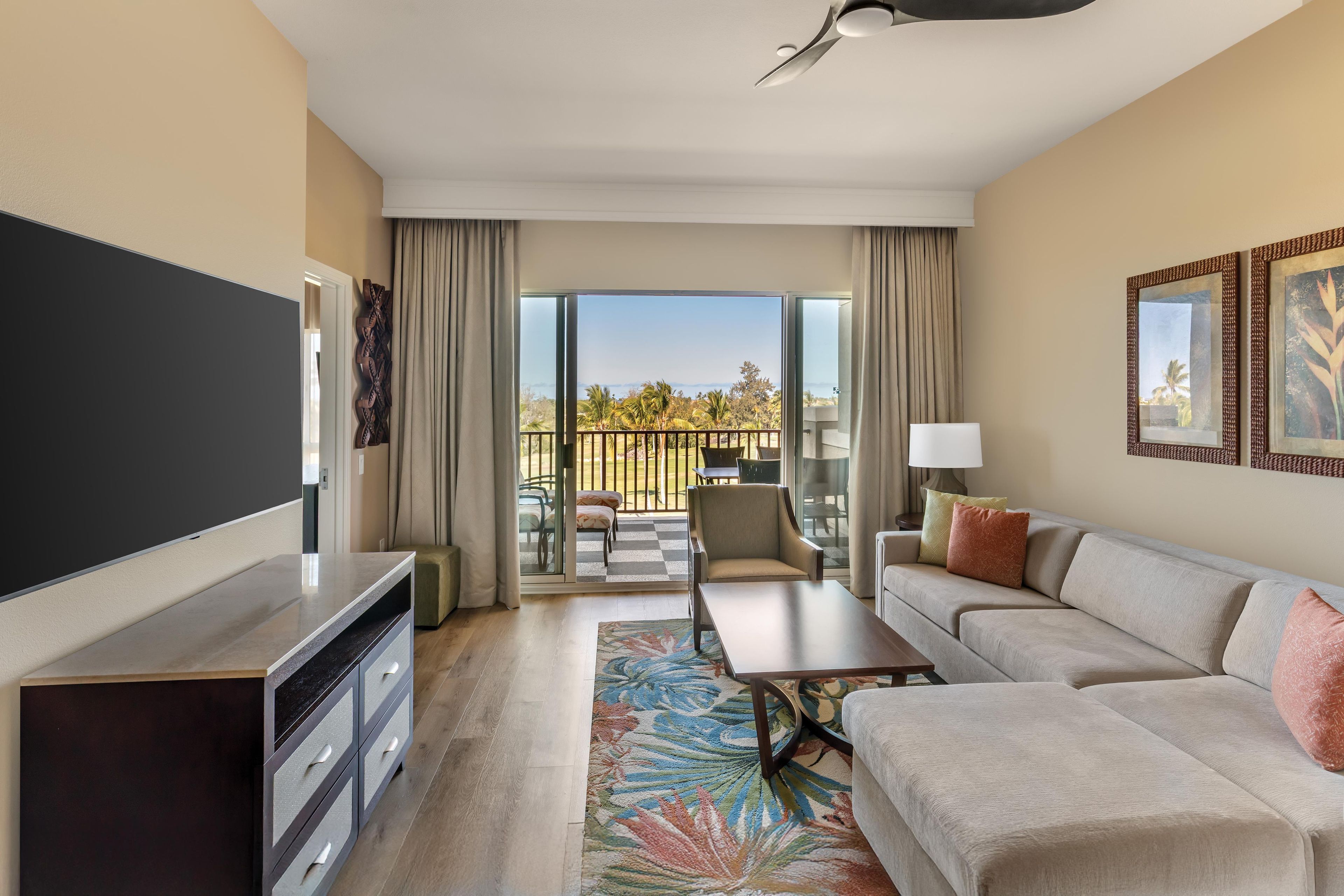 Une chambre d’hôtel dotée d’une télévision à écran plat, d’un canapé, d’une table basse, d’un tapis à motifs et d’un balcon aménagé avec du mobilier d’extérieur.