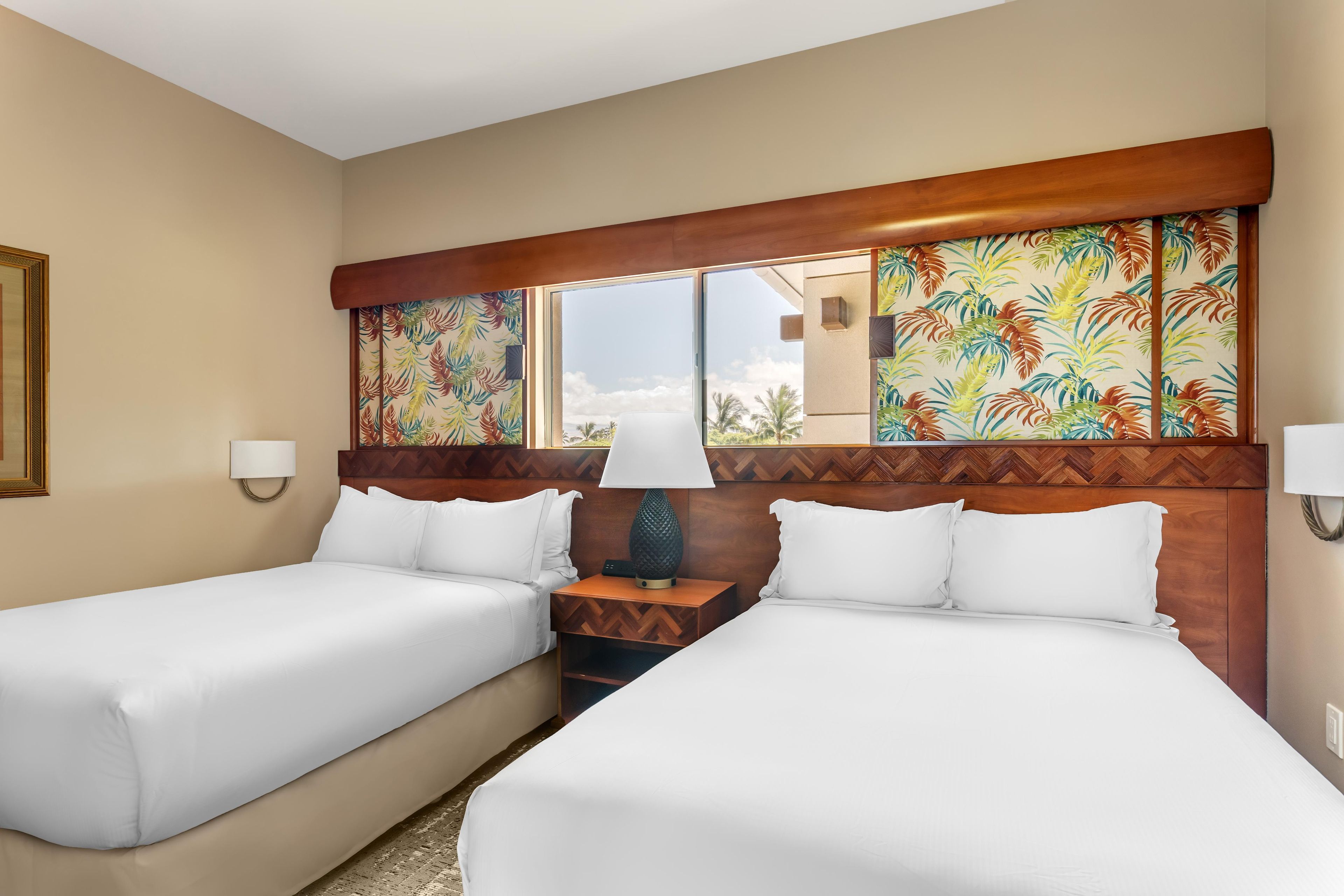 A hotel room with two beds, a wooden headboard, a window with a view, and a nightstand with a lamp.