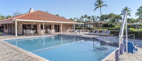 A swimming pool with lounge chairs and a covered area with tables and chairs.