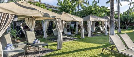 Une série d’espaces de détente en plein air, avec des chaises et des parasols, entourés de palmiers et bordés d’un chemin en pierre.