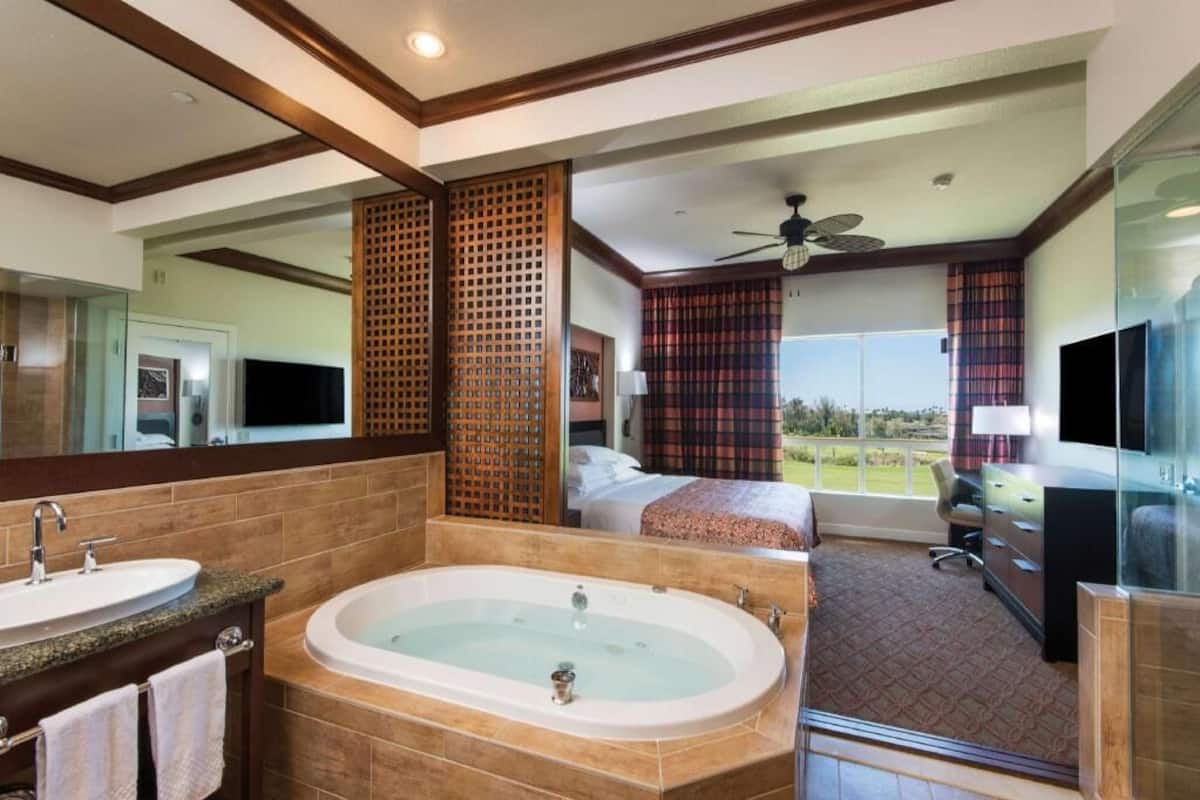 Ein Hotelzimmer mit einer großen Badewanne, einem Bett mit Ausblick, einem Fernseher und einem Balkon.
