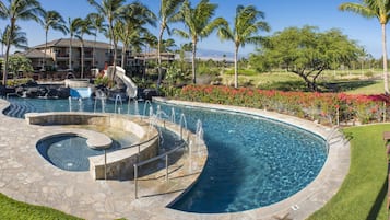 A swimming pool with a waterfall feature, surrounded by palm trees and a golf course in the background.