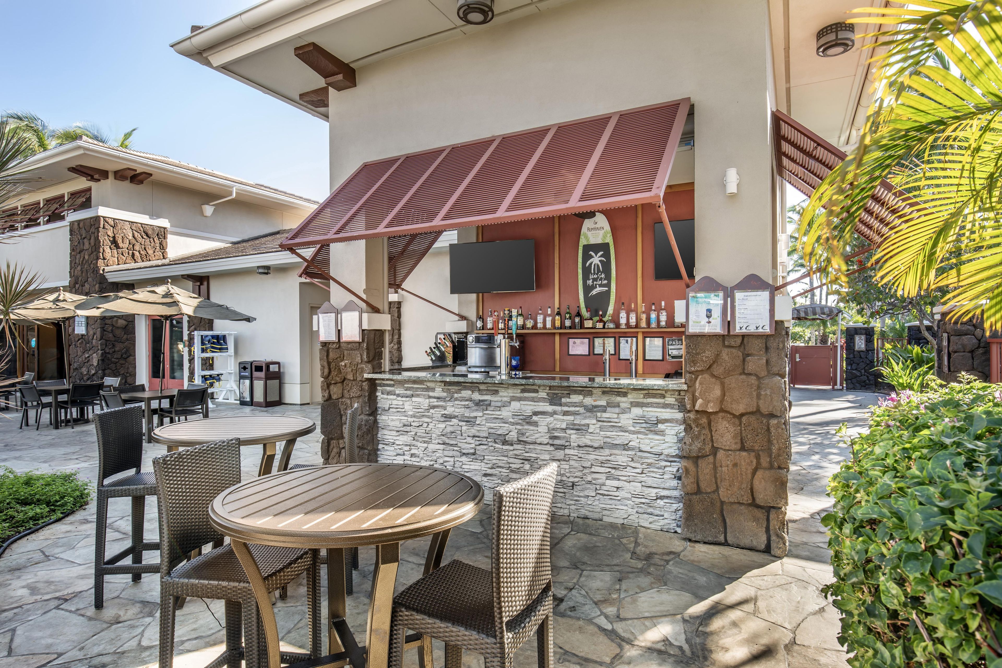 An outdoor bar area with stone walls, wicker furniture, and a flat-screen TV mounted above the bar.