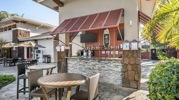 An outdoor bar area with stone walls, wicker furniture, and a flat-screen TV mounted above the bar.