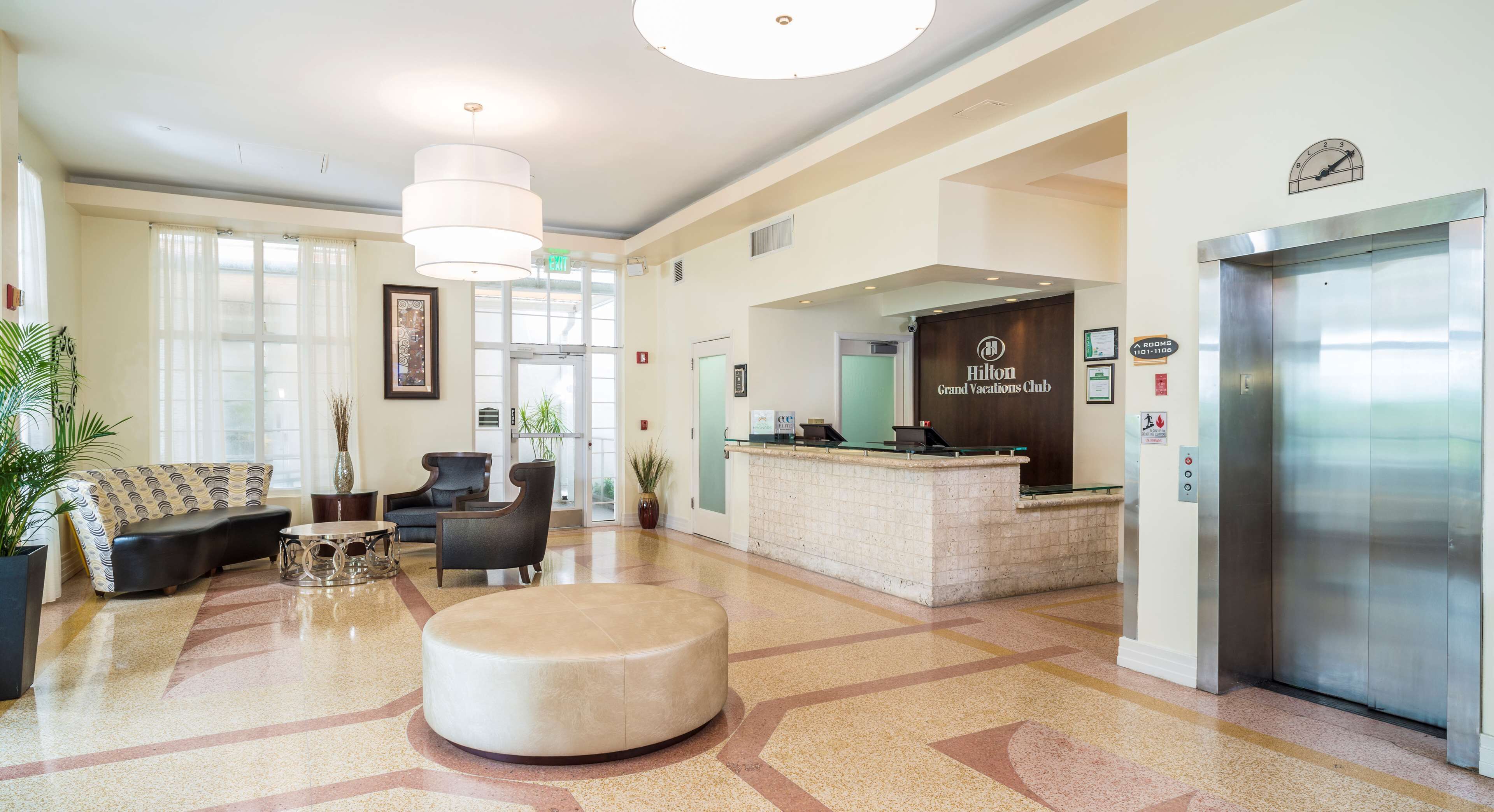 A hotel lobby with a reception desk, a sofa, a coffee table, and an elevator.