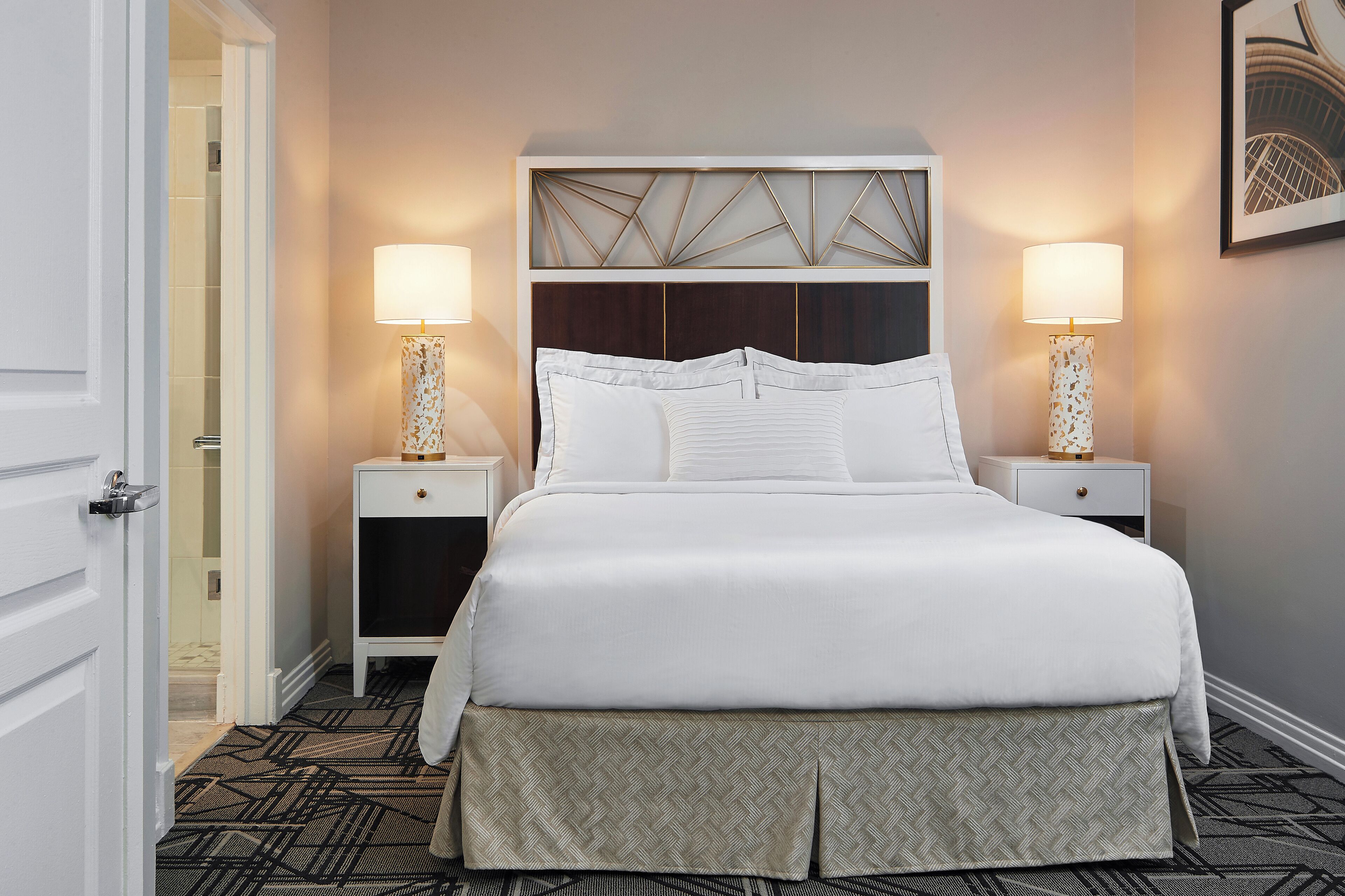 A neatly made bed with white linens, two bedside tables with lamps, and a patterned carpet.