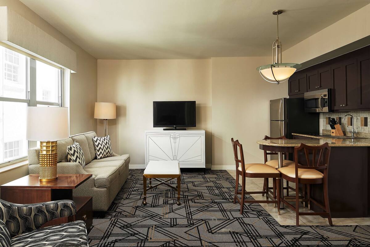 A modern living room with a sofa, a coffee table, a TV, and a kitchen area with a microwave and refrigerator.