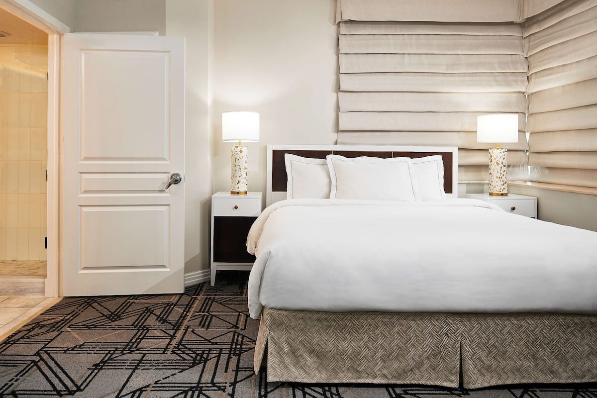 A hotel room with a bed, two bedside tables with lamps, a door, and a patterned carpet.