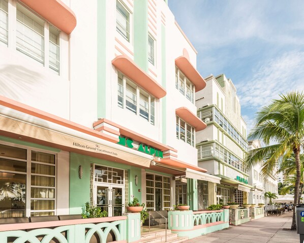 Un hôtel à la façade verte et blanche, avec une enseigne indiquant « Hilton Grand Vacations Club », et des espaces extérieurs aménagés avec des plantes en pot.