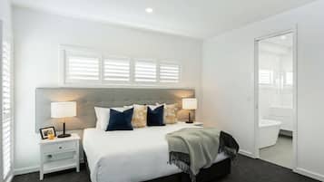 Un dormitorio moderno con una cama grande, mesitas de noche y una ventana con persianas.