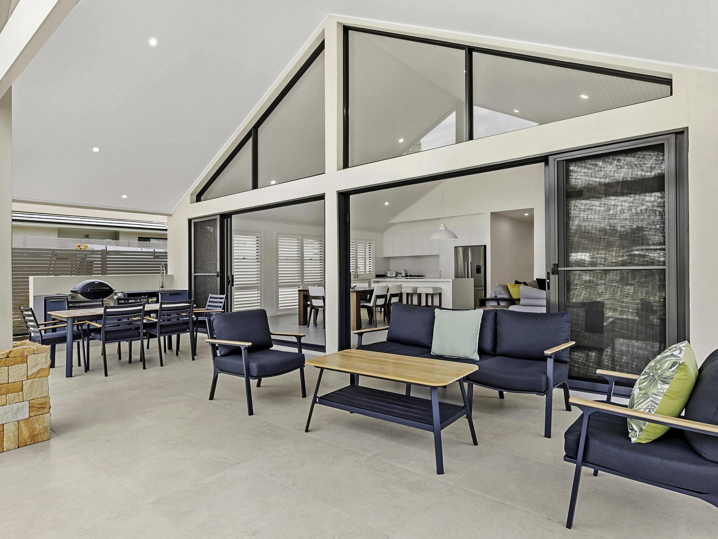 Un interno moderno con zona pranzo, cucina e soggiorno, caratterizzato da ampie finestre e un soffitto alto.