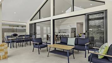 A modern interior with a dining area, kitchen, and living space, featuring large windows and a high ceiling.