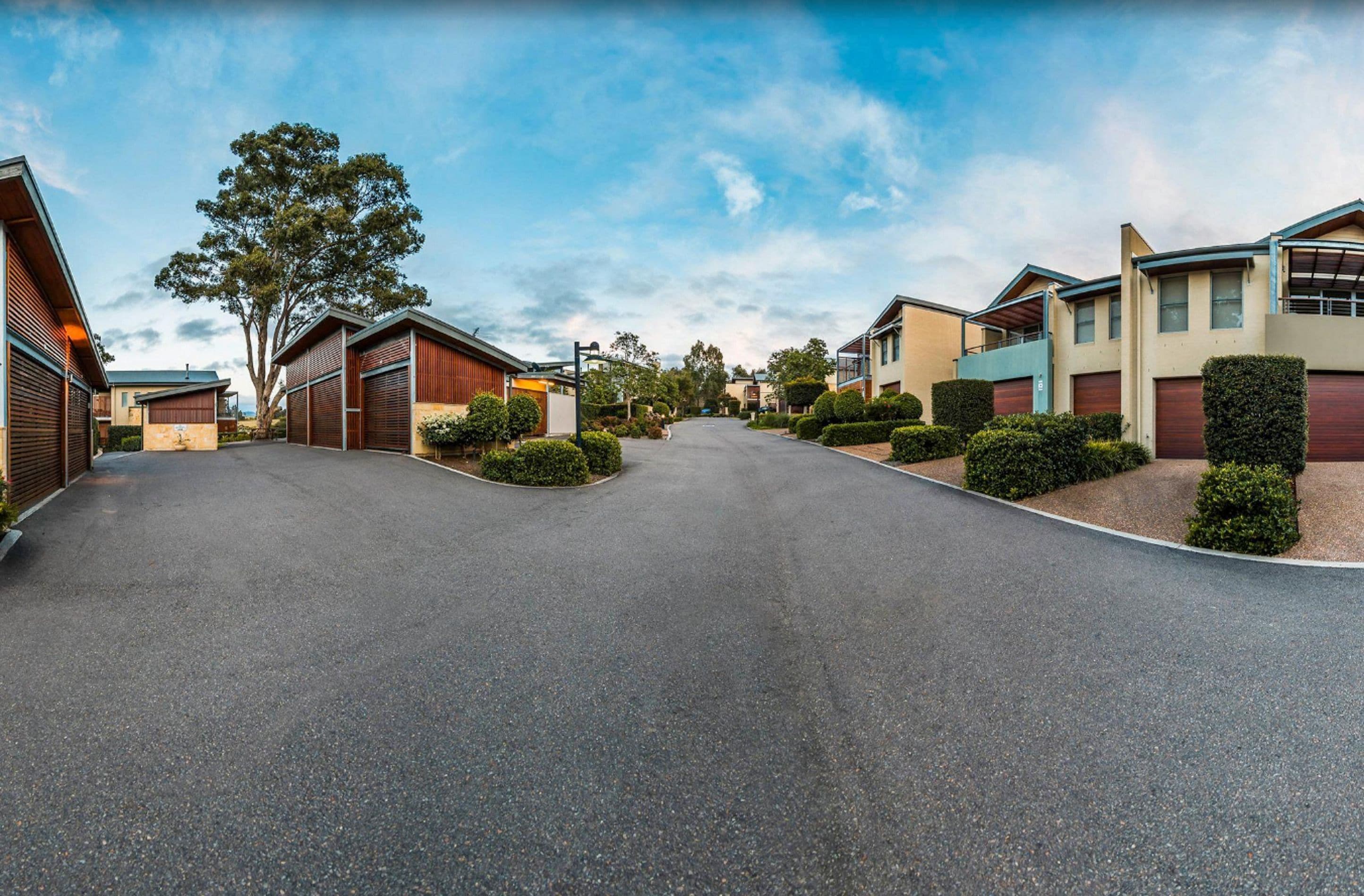 Una calle residencial con casas modernas, cielo despejado y jardines bien cuidados.