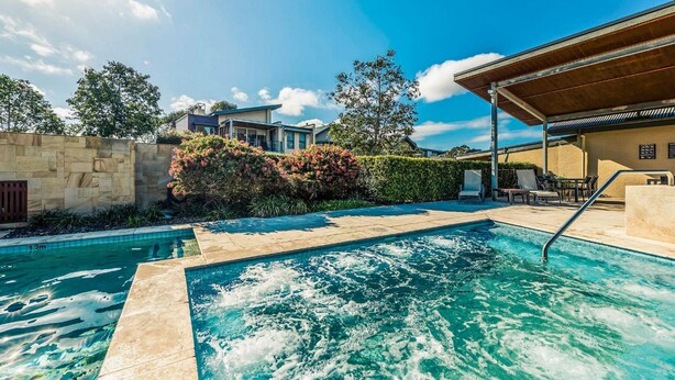 Une piscine bordée de pierres, un patio couvert avec des sièges et un mur en pierre.