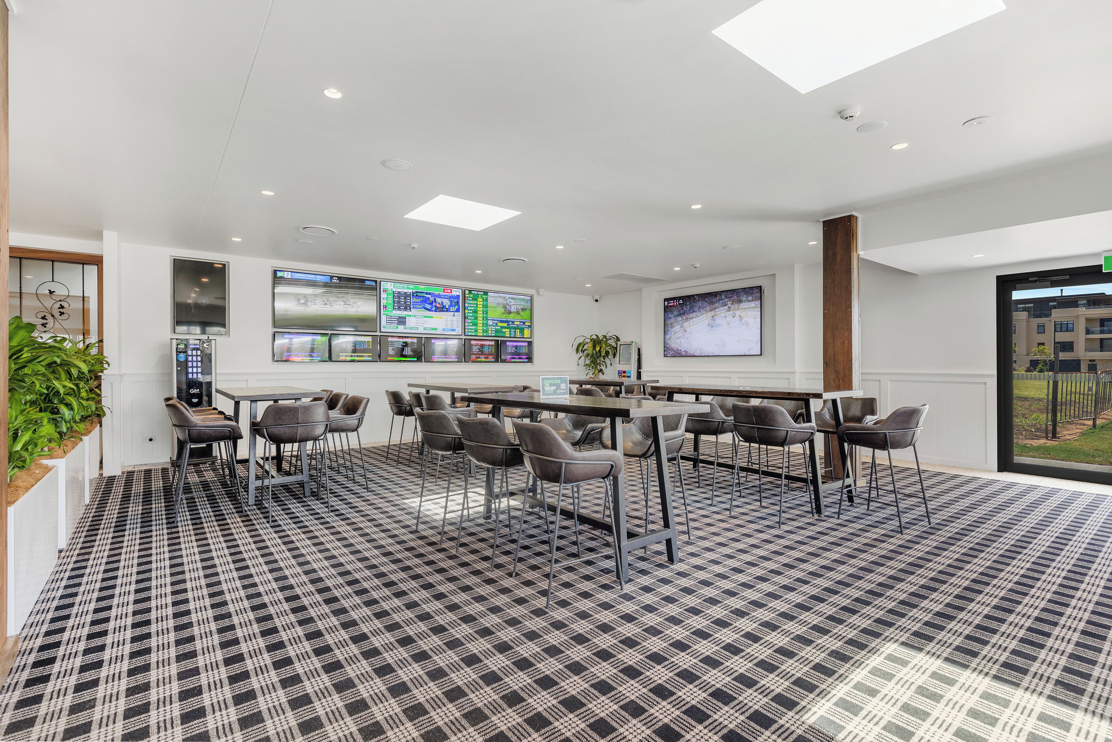 Een moderne hotellobby met een receptiebalie, verschillende zithoeken en grote digitale schermen aan de wanden.