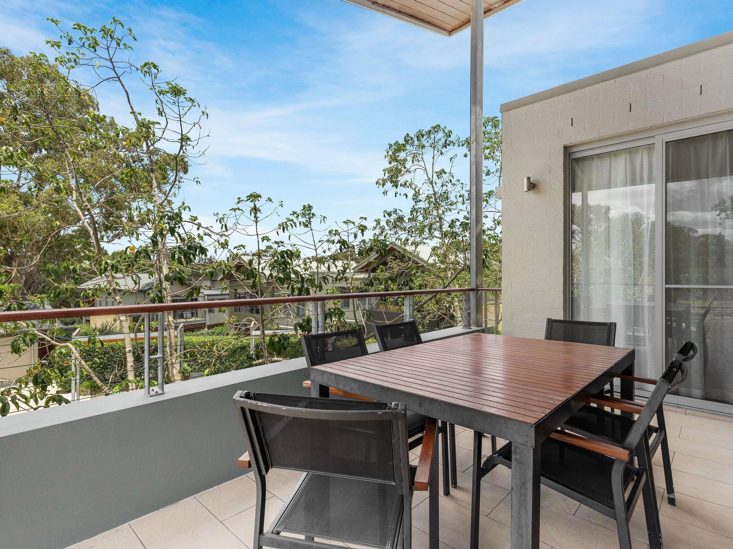 A balcony with a table and chairs, a railing, and a view of trees and buildings.