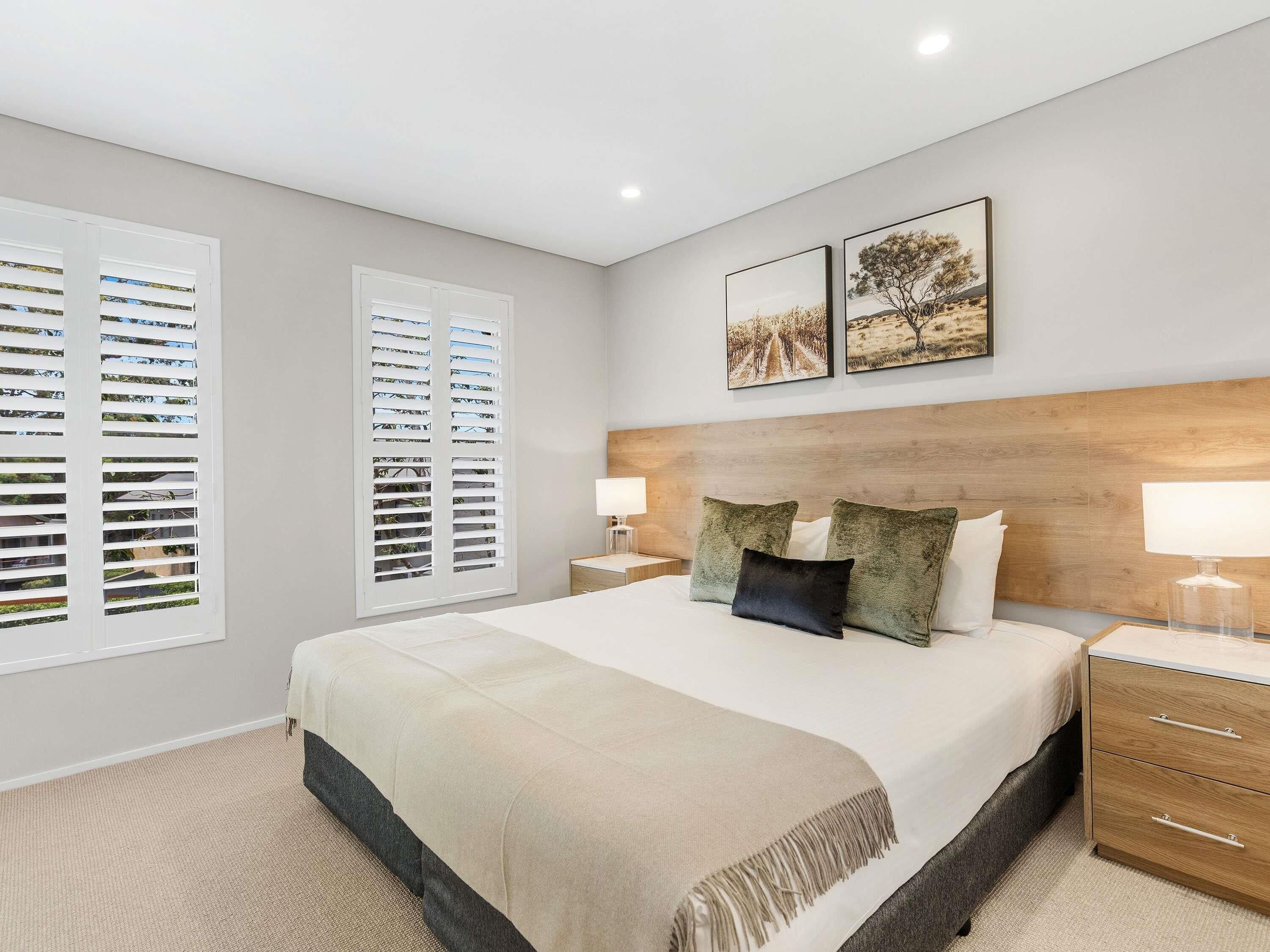 A bedroom with a large bed, two bedside tables, a headboard, and two wall-mounted pictures.