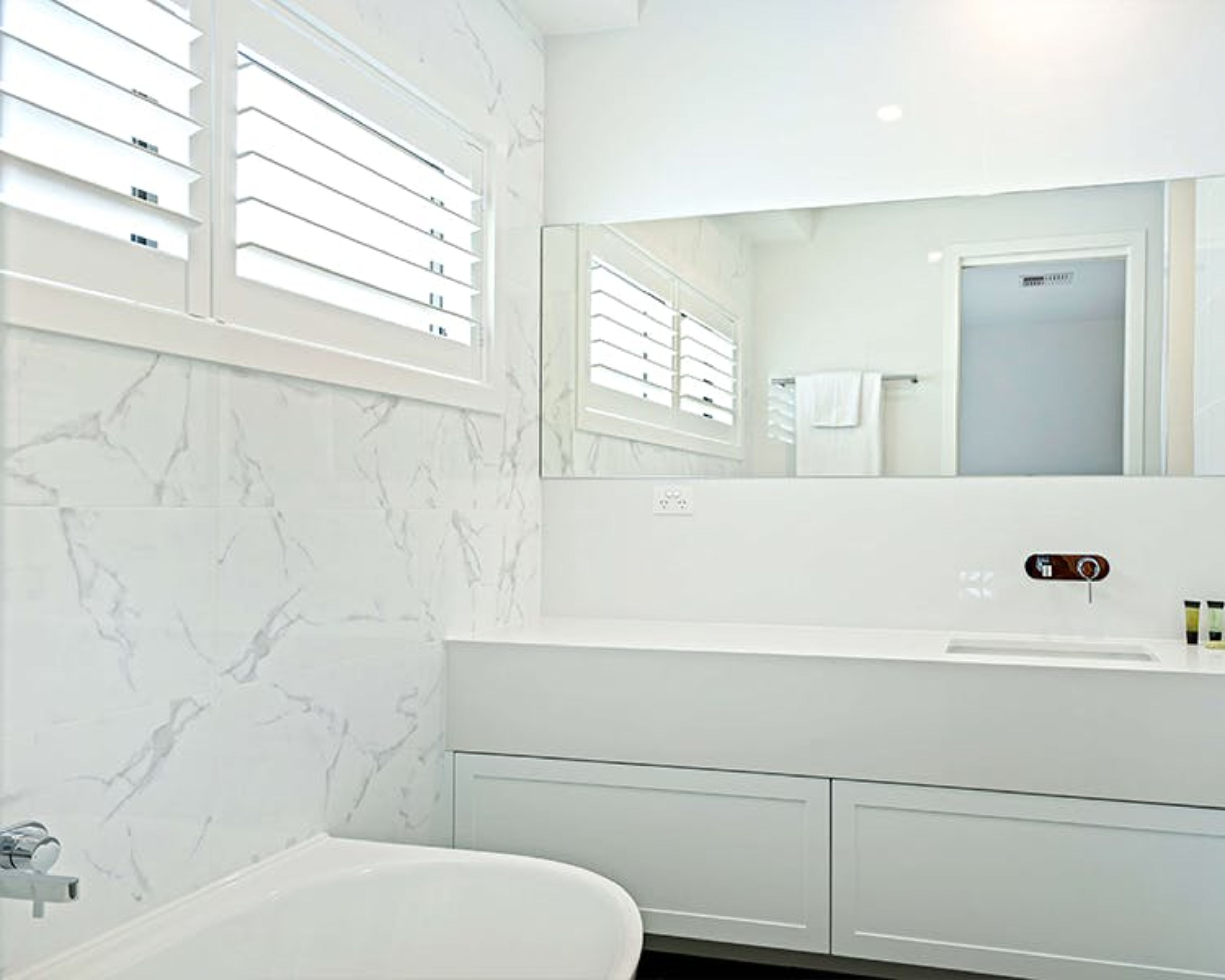 Un baño moderno con pared de mármol, un lavabo blanco y un espejo grande.