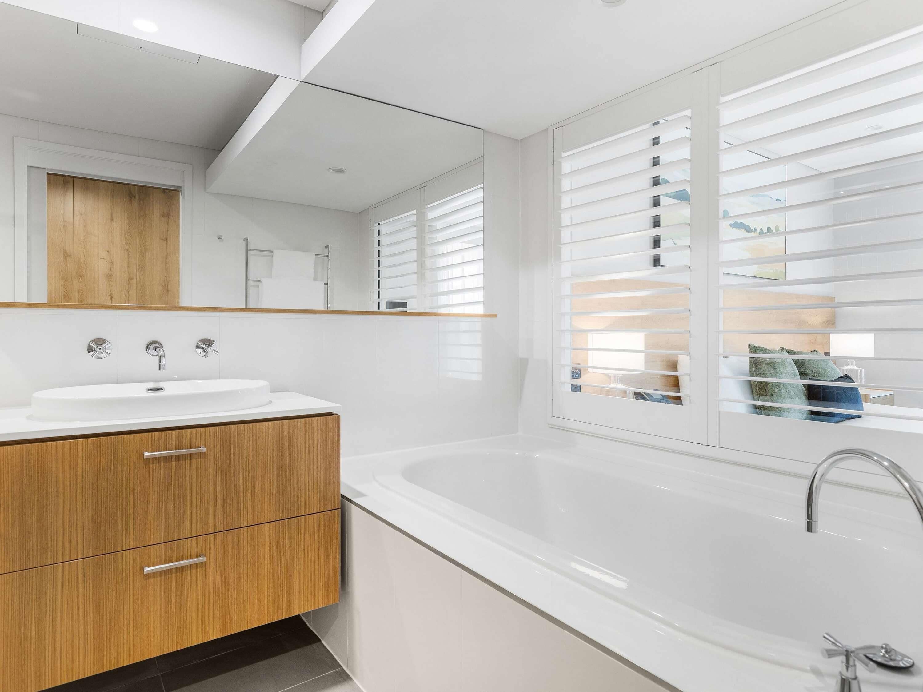 A modern bathroom with a white sink, wooden vanity, and a large bathtub.
