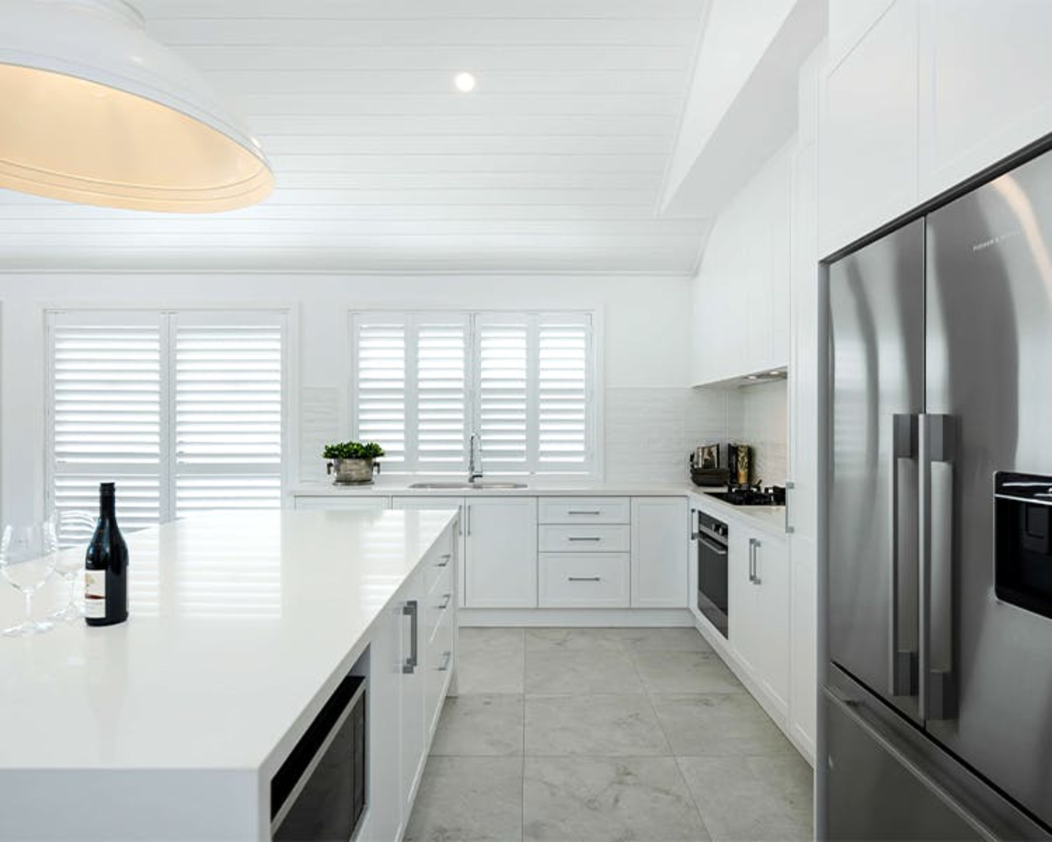 Una cocina moderna con armarios blancos, una isla grande, electrodomésticos de acero inoxidable y una lámpara colgante.