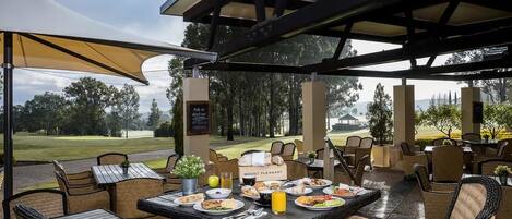 An outdoor dining area with wicker furniture and a table set with plates, glasses, and a pitcher of orange juice.