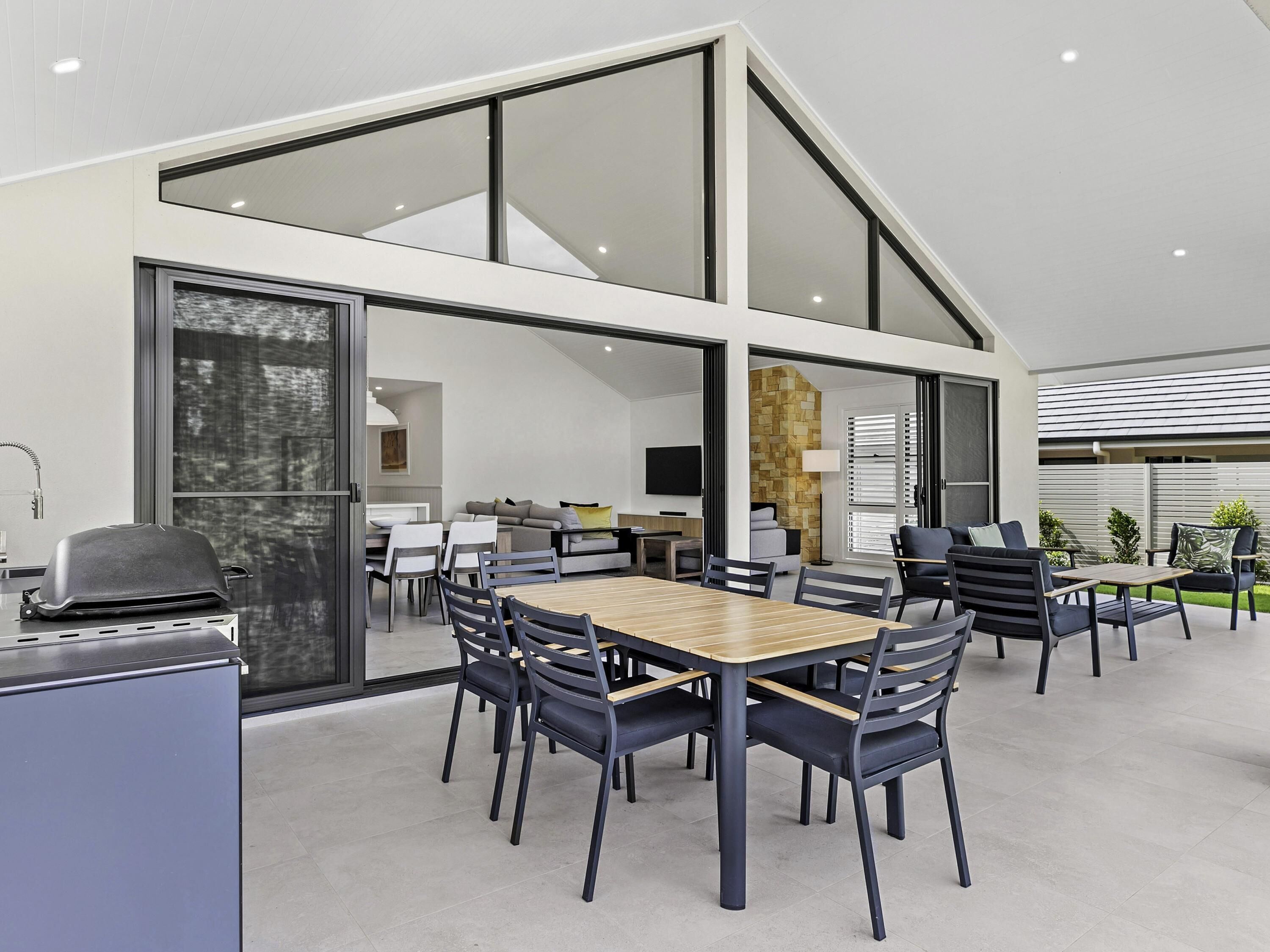 Un espace repas moderne avec une grande table et des chaises, un barbecue et une vue sur l’intérieur.