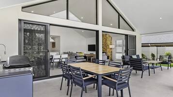Un espace repas moderne avec une grande table et des chaises, un barbecue et une vue sur l’intérieur.