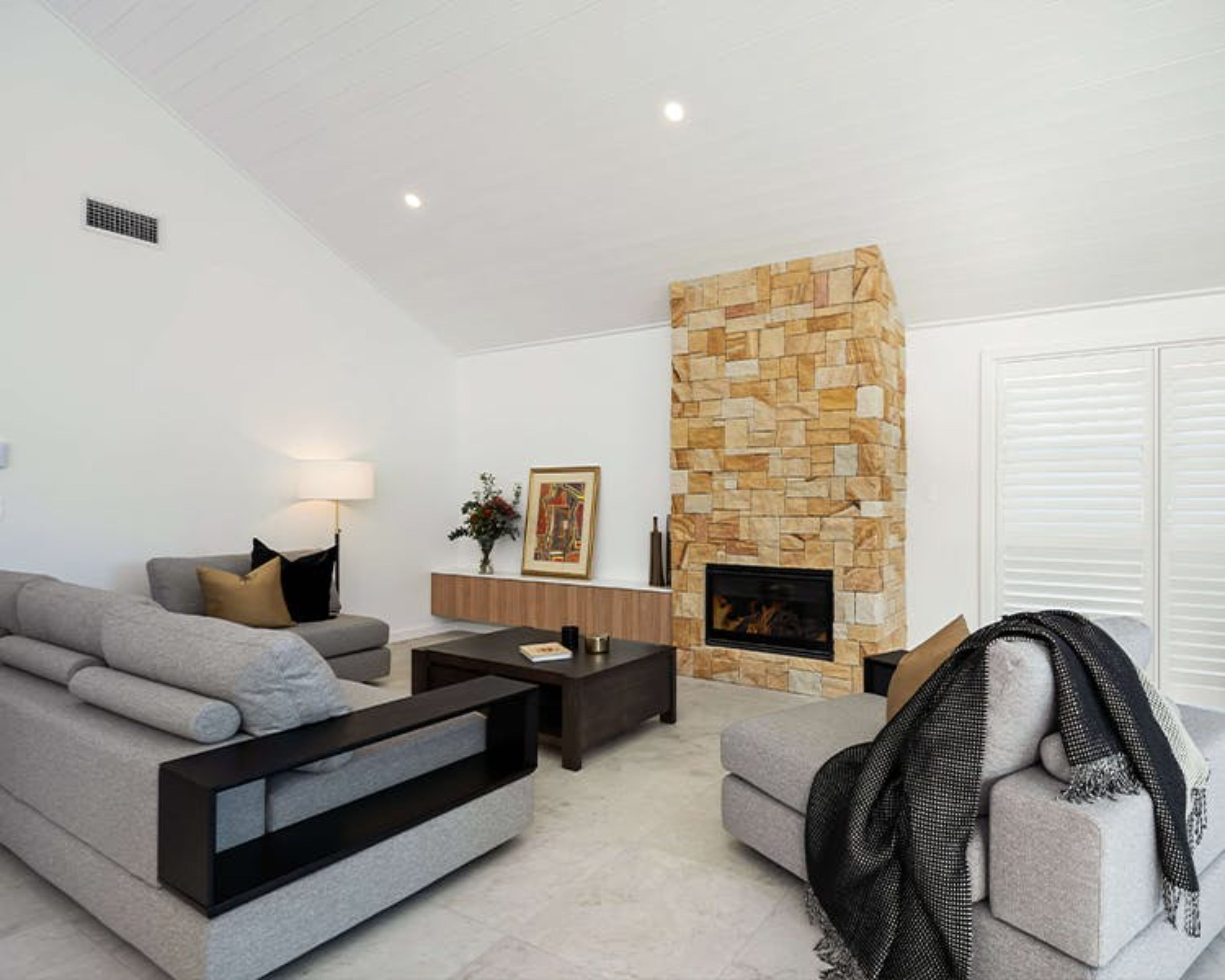A modern living room with a stone fireplace, grey sofas, a coffee table, and a lamp.