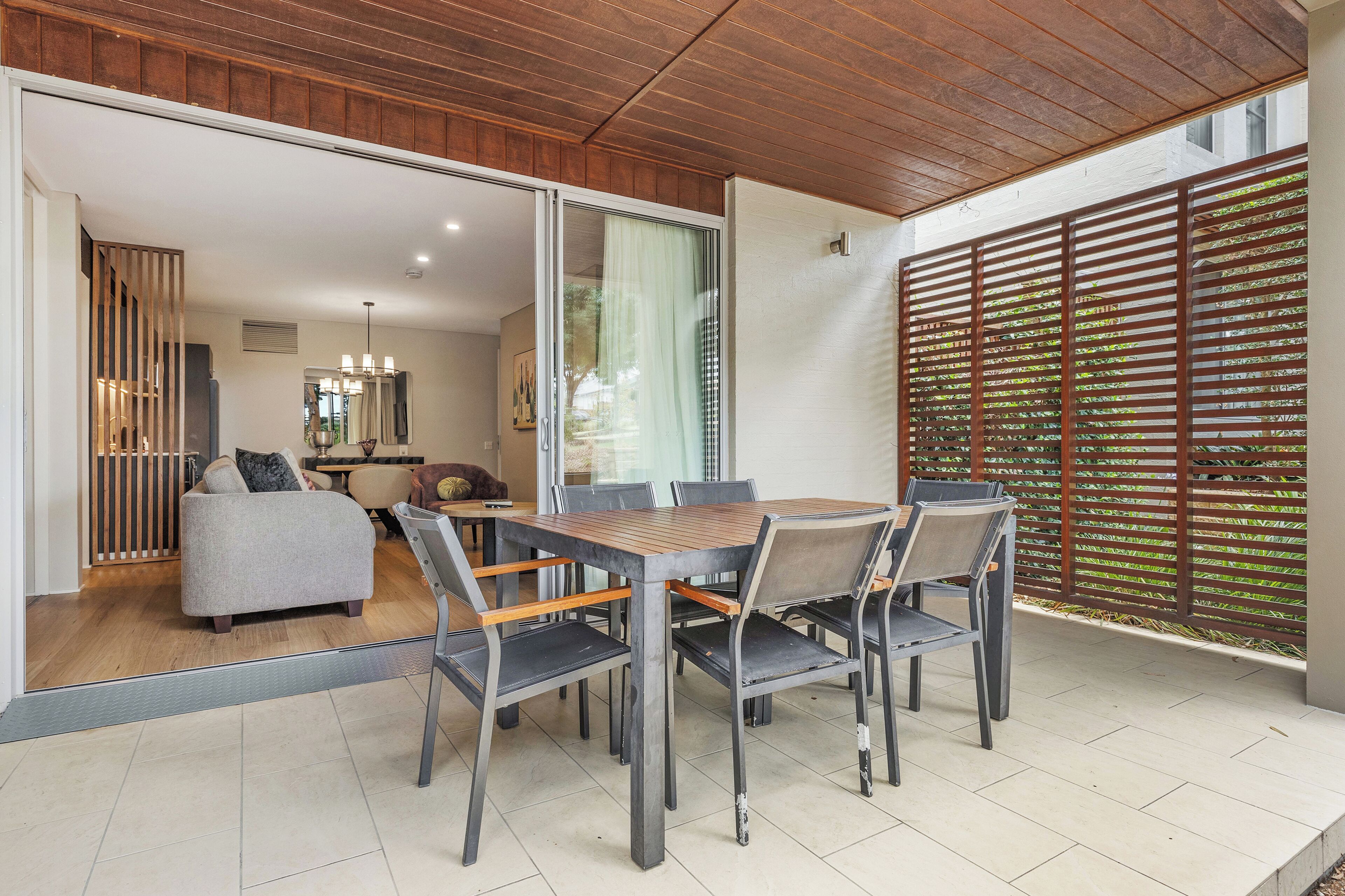 Un espace repas moderne avec une table et des chaises en bois, un canapé gris et une porte-fenêtre coulissante donnant sur un salon.