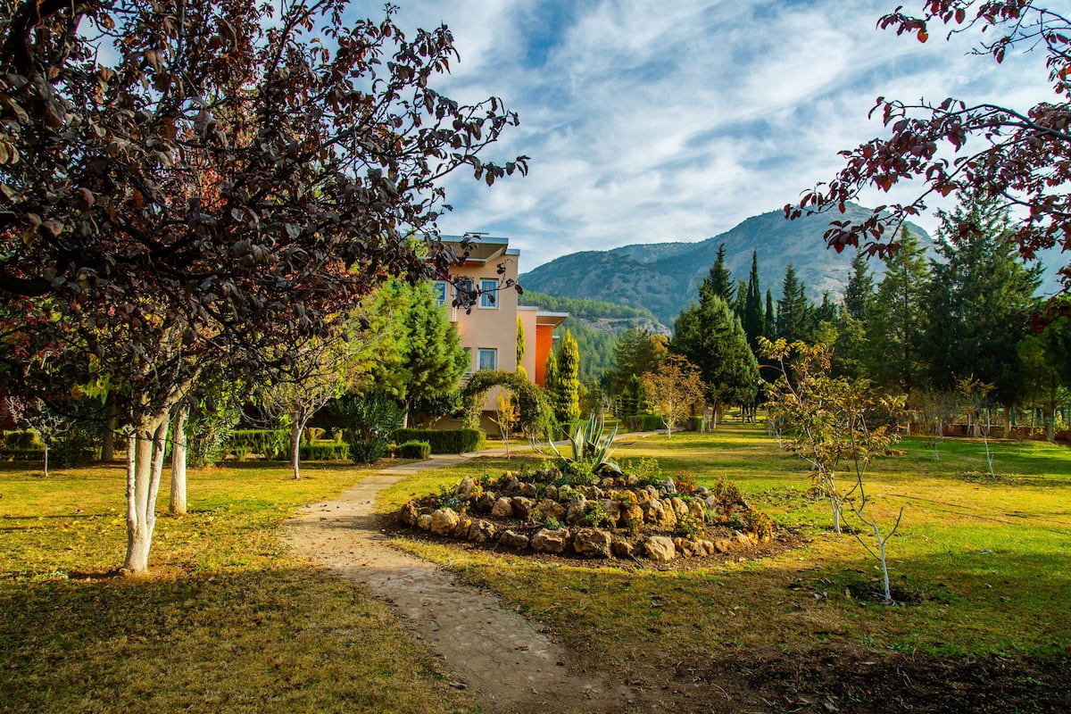 A pathway leading to a building surrounded by trees and a mountainous backdrop.