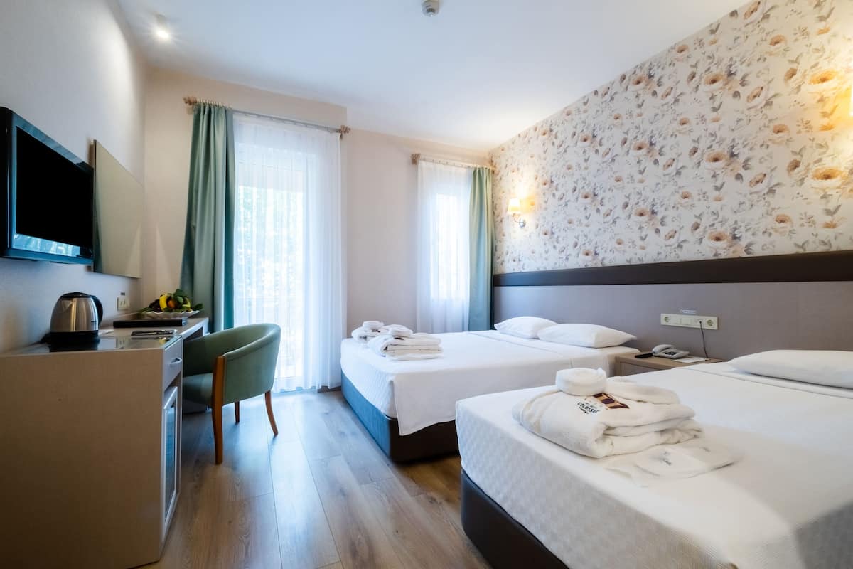 A hotel room with two beds, a desk, a chair, a TV, and a floral wall.
