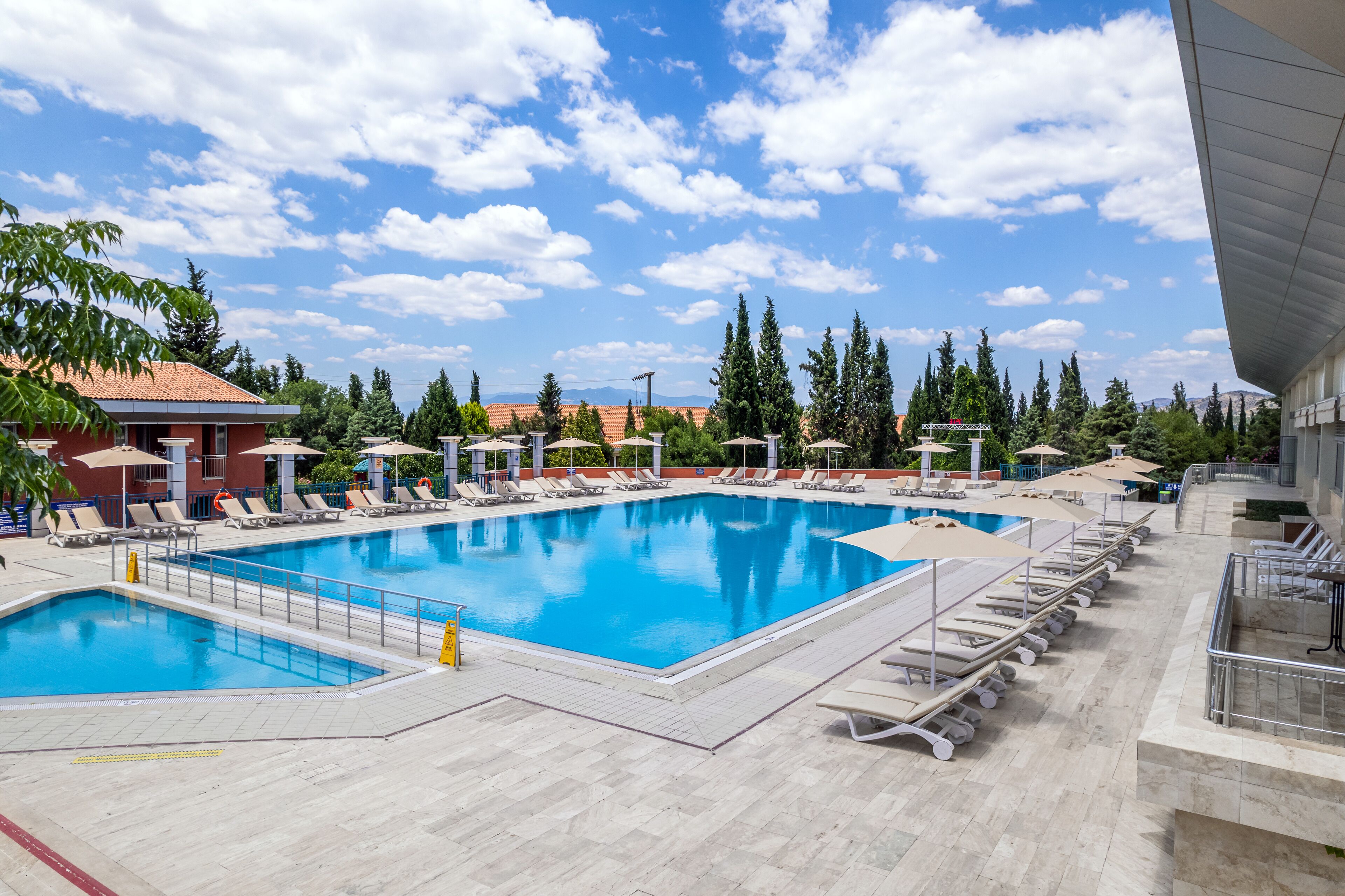 Una gran piscina al aire libre con múltiples sillas de descanso y sombrillas, rodeada de árboles y edificios.