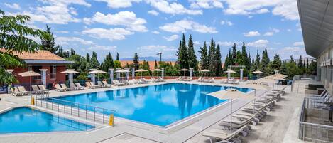 Una gran piscina al aire libre con múltiples sillas de descanso y sombrillas, rodeada de árboles y edificios.