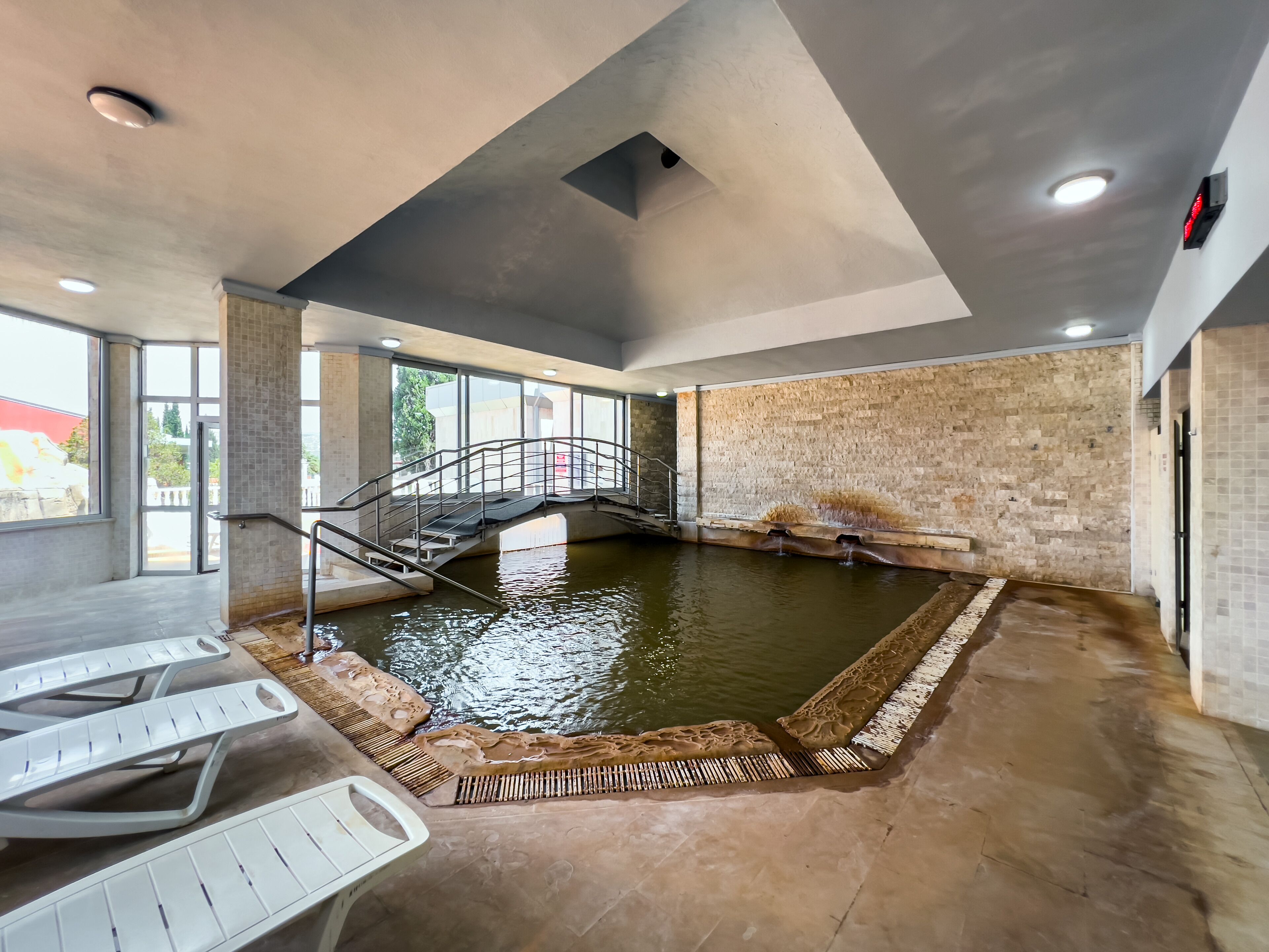 Un área de piscina interior con una pared de piedra, un puente y vistas al exterior.