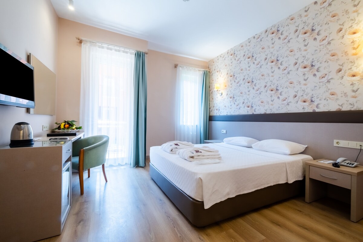 A hotel room with a bed, bedside table, desk, chair, and a TV.