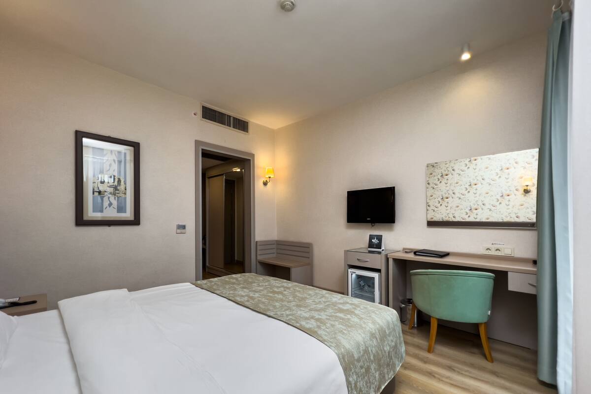 A hotel room with a bed, a desk with a computer, a chair, a TV, and a mirror.
