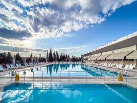 A swimming pool with lounge chairs and a covered area, surrounded by trees and a building.
