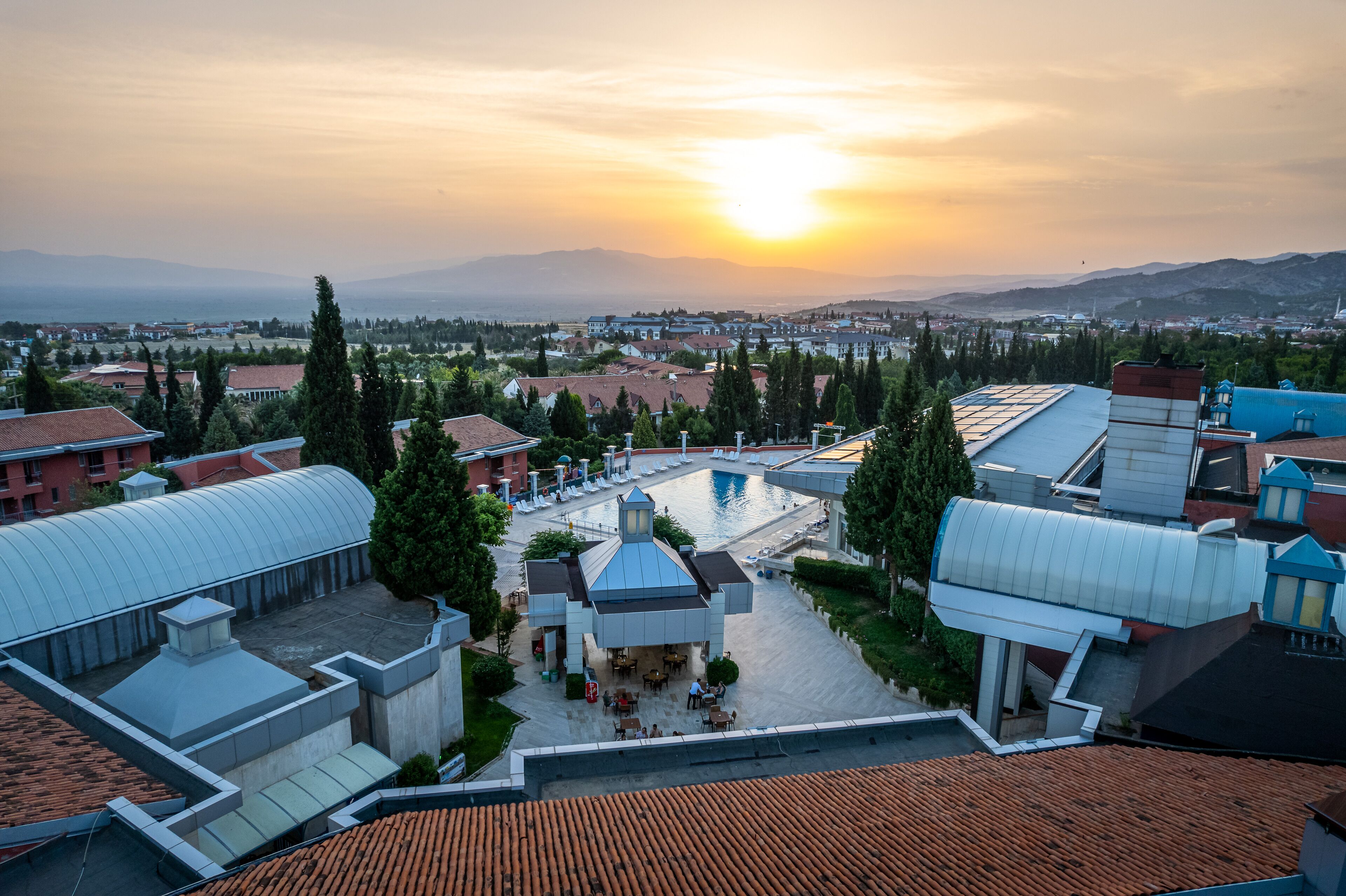 Une cour d’hôtel avec une piscine, entourée de bâtiments et d’arbres, au coucher du soleil.