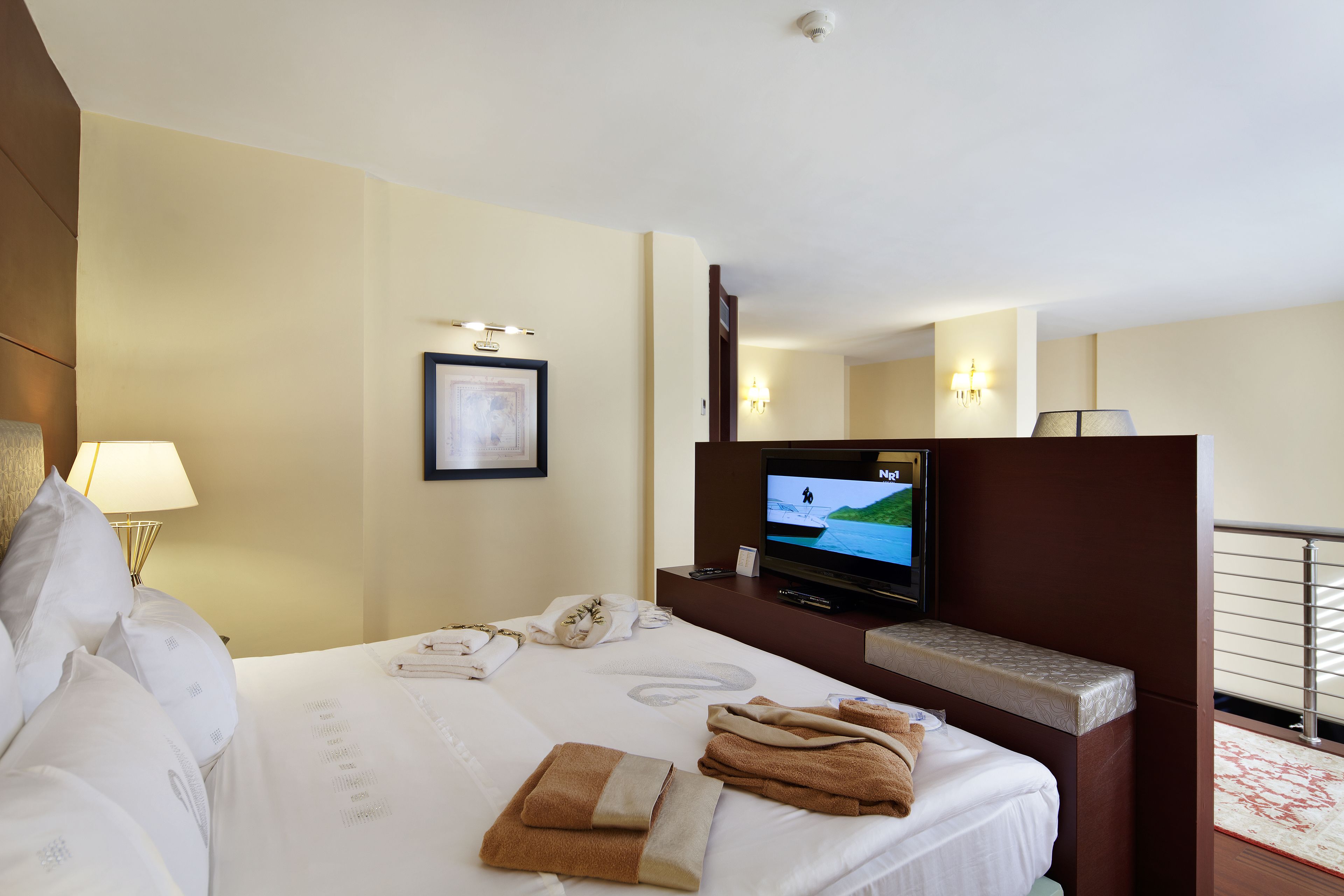 Une chambre d’hôtel avec un lit, une télévision, un bureau avec une lampe et un tableau encadré au mur.