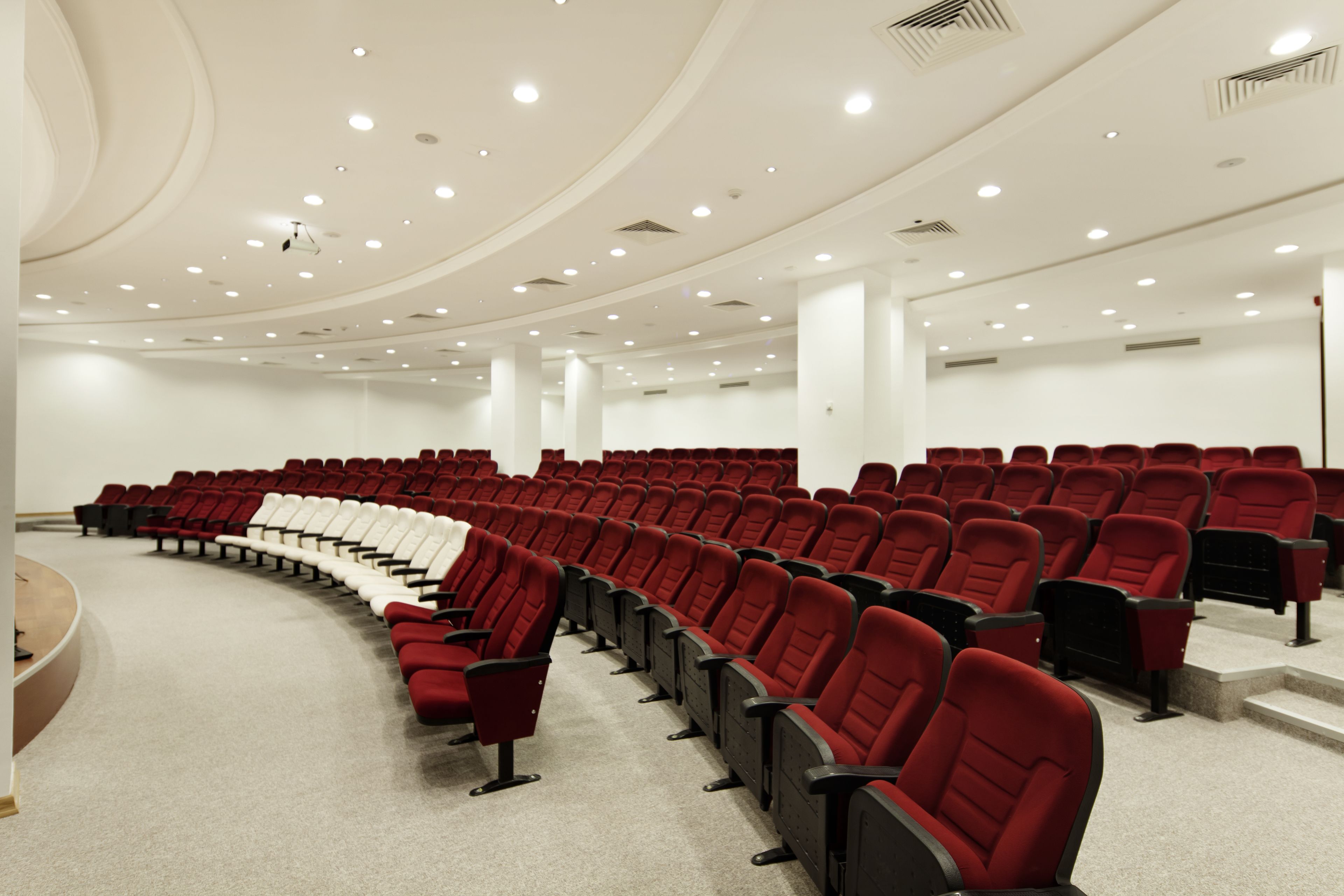 Un amplio auditorio con hileras de sillas rojas y negras, paredes blancas y un techo curvo con iluminación empotrada.