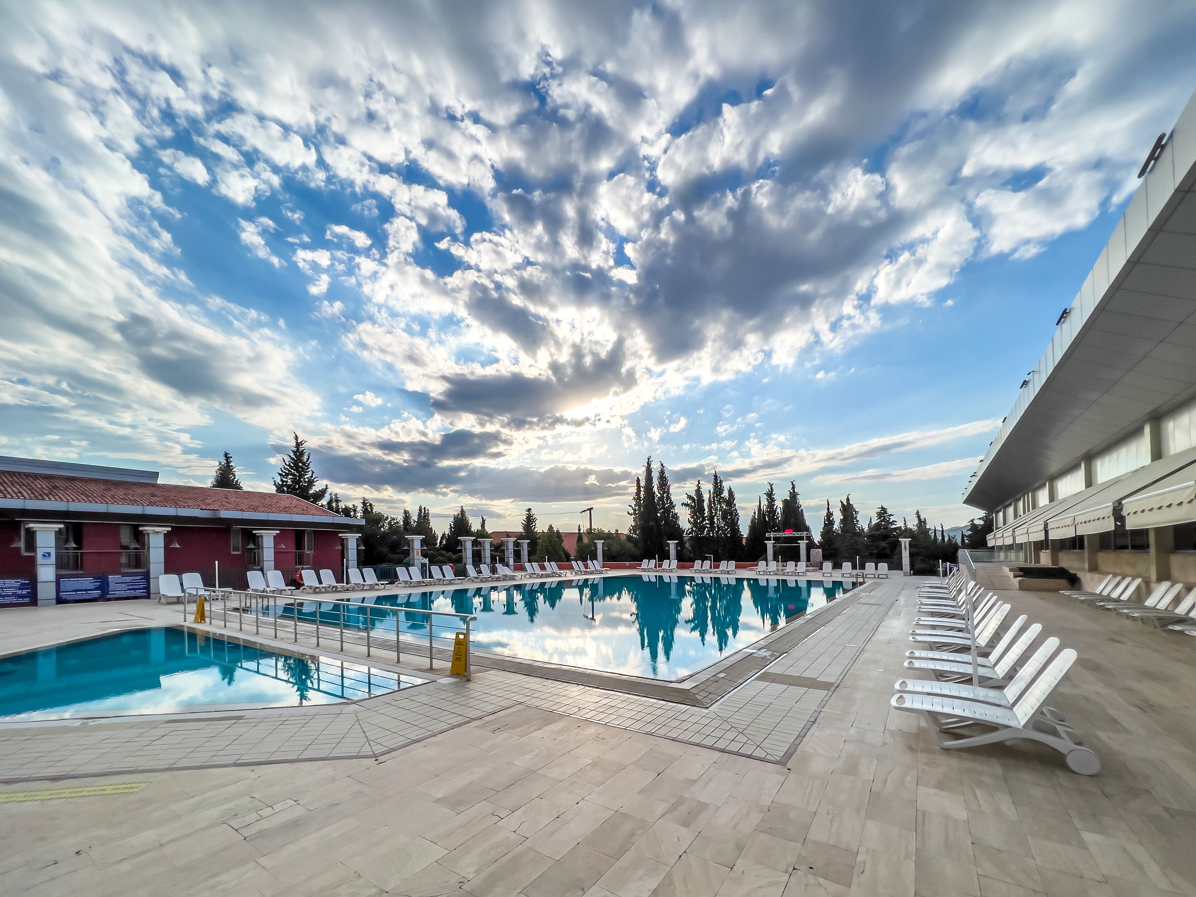 Una piscina con sillas de descanso y un edificio de techo rojo al fondo.