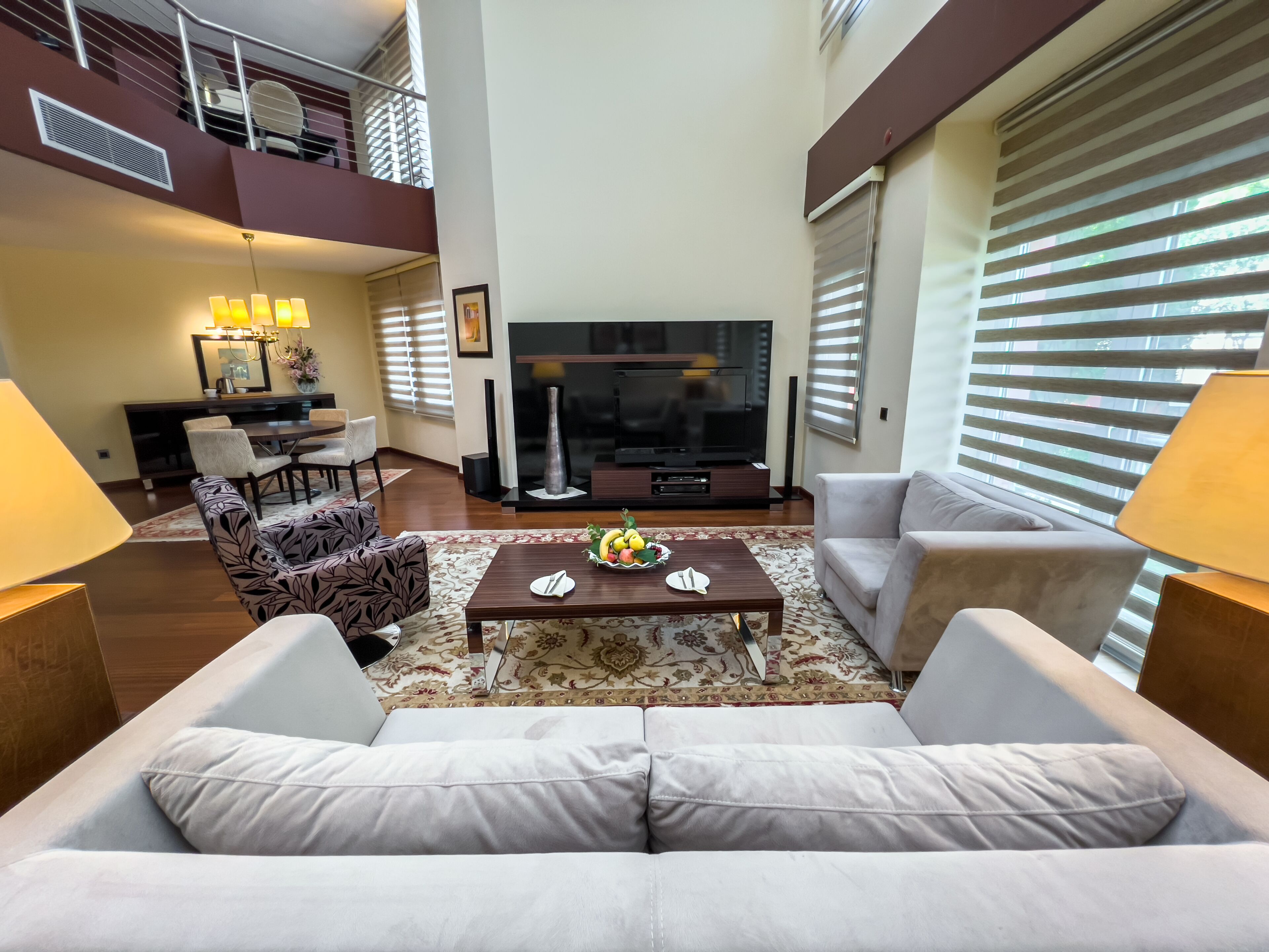 A modern living room with a sofa, coffee table, and TV. There is a balcony with outdoor furniture.