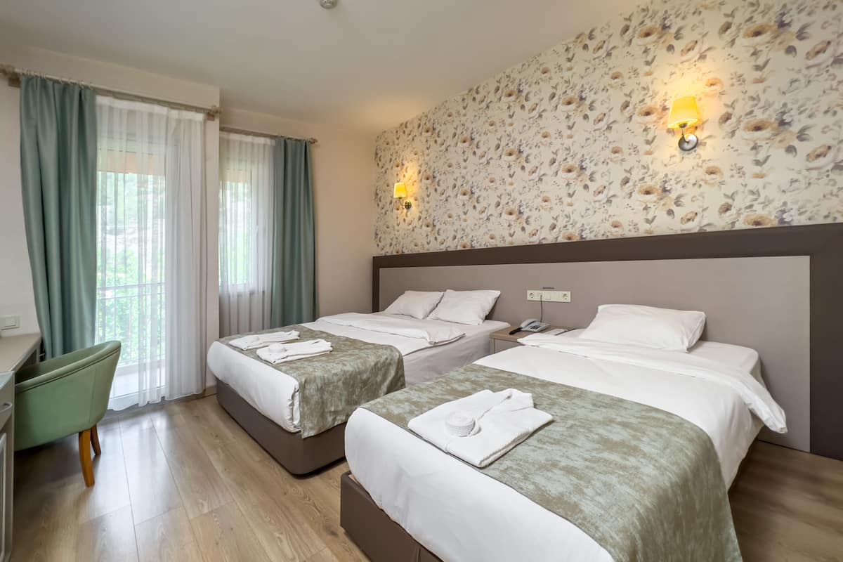 A hotel room with two beds, a desk, and a green chair.