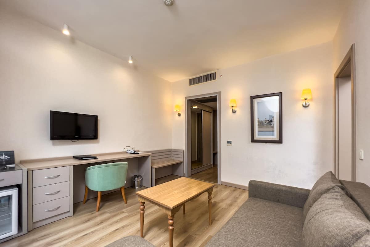 A compact living space with a kitchenette, a sofa, a wooden table, and a TV mounted on the wall.