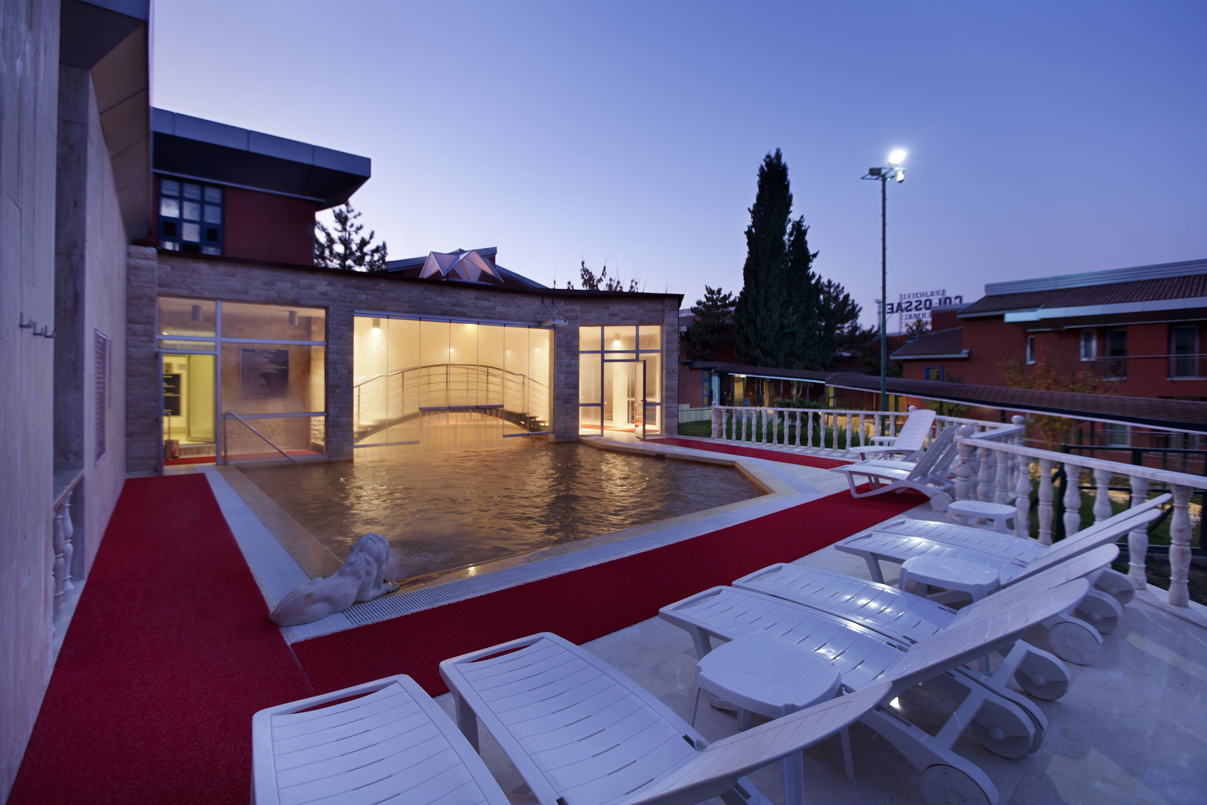 A swimming pool with a red carpet, white lounge chairs, and a building with a glass facade.