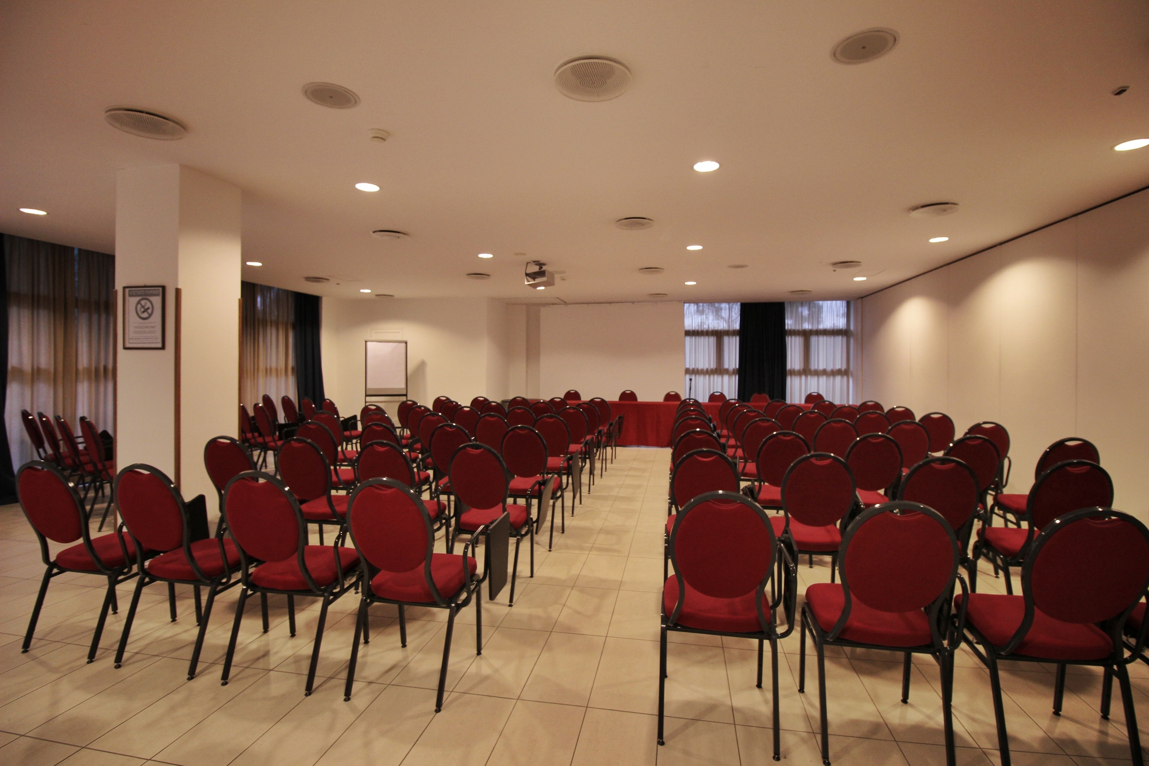 A conference room with rows of red chairs, a whiteboard, and a projector screen.